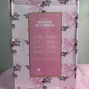 Puede incluir: Una caja de cart&oacute;n rectangular para un vaso Flowstate Quencher H2.0 de 1,18 L. La caja presenta un fondo rosa claro con un patr&oacute;n repetitivo de lazos rosas y peque&ntilde;os detalles florales rojos y verdes. Una gran etiqueta rosa central muestra los detalles.