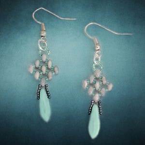 May include: A pair of silver earrings with a geometric design made of light blue and white beads. The earrings have a teardrop-shaped pendant at the bottom.