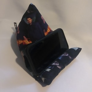 May include: A black and blue phone stand with a printed image of a man in front of flames. The stand is made of fabric and has a pocket for holding a phone.
