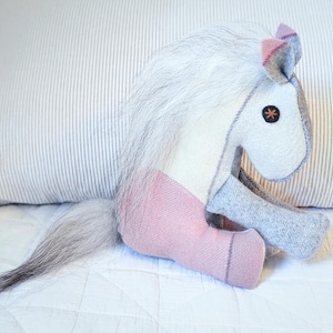 May include: A plush toy horse with a white body, pink legs, and a gray tail. The horse has a black star on its face and a pink and gray ear.
