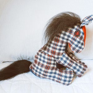 Puede incluir: Un caballo de peluche con un patrón de cuadros blanco y negro y detalles rojos. El caballo tiene una cola y una crin negras largas.