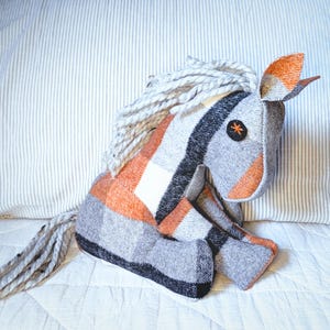 May include: A gray and orange stuffed horse toy with a white mane and tail. The horse has a black stripe down its back and a black button eye.
