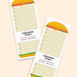 May include: Two white notepads with a burger design at the top. Each notepad has a yellow sesame seed bun, red tomato, and cheese. The notepads have lines and check boxes. The text "raisukeik designs" and "50 SHEET NOTEPAD 3 ½ x 8 ½ in | 89 x 216 mm" are visible.