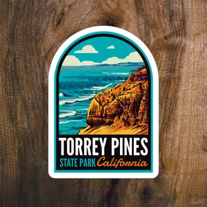 May include: A white sticker with a blue and orange illustration of a cliff overlooking a blue ocean with white waves. The sticker says "Torrey Pines State Park California".