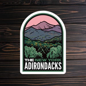 May include: A sticker with a white border and a green and purple mountain landscape with a pink sky. The text "THE NEW YORK ADIRONDACKS" is printed in white on a green background.