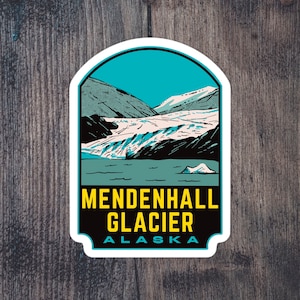 May include: A sticker featuring a scenic illustration of Mendenhall Glacier in Alaska. The design includes a turquoise sky, snow-capped mountains, and the glacier itself, with the text "Mendenhall Glacier Alaska" in bold yellow letters.