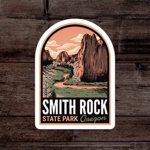 May include: A sticker featuring a landscape illustration of Smith Rock State Park in Oregon. The design includes a river, mountains, and a sunset sky. The text "Smith Rock State Park Oregon" is displayed in a bold font.