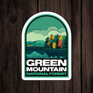 May include: A sticker with a green, blue, and white design of a lake and trees in a mountain landscape. The text "GREEN MOUNTAIN NATIONAL FOREST" is printed in white on a green background.