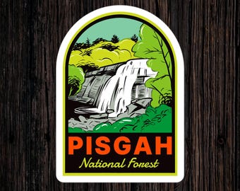 Pode incluir: Um autocolante com uma cena de cachoeira dentro de uma borda arqueada verde, preta e amarela. O texto "PISGAH National Forest" é exibido em laranja e branco. O design evoca uma estética de viagem vintage.