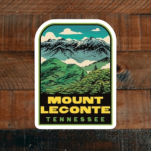May include: A vintage-style sticker featuring a scenic view of Mount LeConte in Tennessee. The sticker depicts a mountain range with snow-capped peaks, lush green forests, and a blue sky with white clouds. The text "MOUNT LECONTETENNESSEE" is printed in yellow letters on a black background.