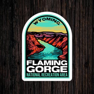 May include: A sticker featuring a colorful illustration of Flaming Gorge National Recreation Area in Wyoming. The sticker shows a canyon with a river flowing through it, with the text "Flaming Gorge National Recreation Area" and "Wyoming" on the sticker.