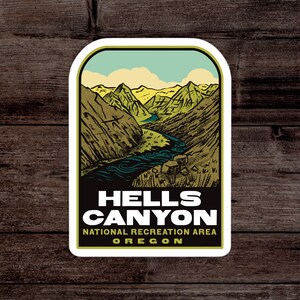 May include: A vintage-style sticker featuring a scenic view of Hells Canyon National Recreation Area in Oregon. The sticker depicts a river winding through a canyon with mountains in the background. The text "HELLS CANYON NATIONAL RECREATION AREA OREGON" is printed in white on a green background.