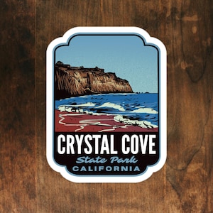 May include: A sticker featuring a scenic view of Crystal Cove State Park in California. The design includes a blue sky, ocean waves, and a brown cliffside. The text "CRYSTAL COVE STATE PARK CALIFORNIA" is prominently displayed in white and black.