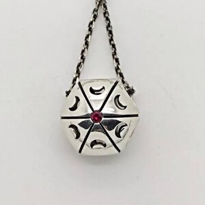 May include: A silver necklace with a hexagonal pendant featuring a red gemstone and crescent moon designs.