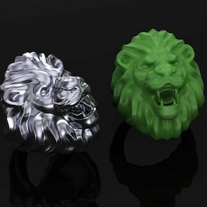 May include: Two lion head rings, one silver and one green. The rings are on a black background.