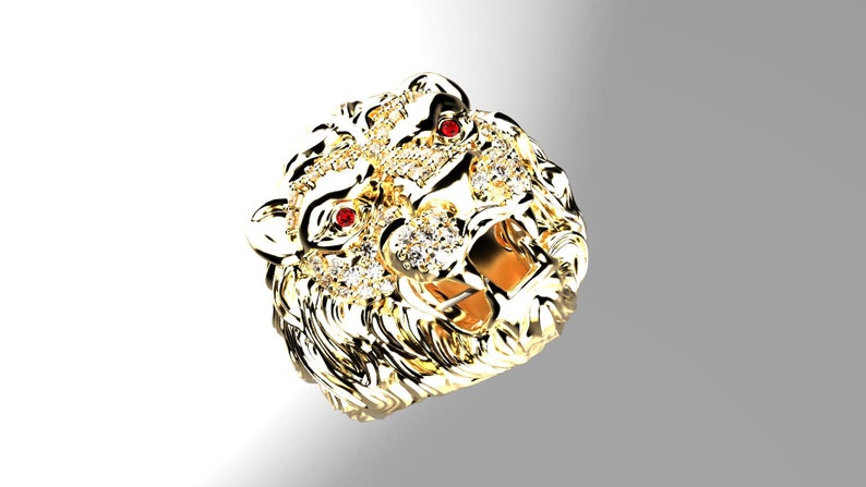 May include: A gold lion head ring with red ruby eyes and a detailed design. The ring is set with clear diamonds.