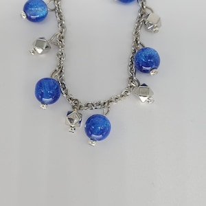 May include: A silver chain bracelet with blue glass beads and silver charms. The bracelet has a lobster claw clasp.