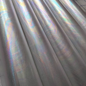 May include: Close-up of iridescent silver fabric with a subtle textured pattern. The fabric has a shimmering, holographic effect.