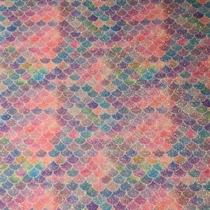 May include: A close-up of iridescent mermaid scale fabric with a glittery finish. The fabric features a repeating pattern of overlapping scales in shades of pink, blue, purple, and green.