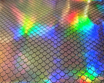May include: A close-up of iridescent mermaid scale fabric with a rainbow pattern. The fabric has a textured, scaly surface and reflects light in a variety of colors.