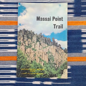 May include: A vintage brochure for the Massai Point Trail in Chiricahua National Monument, Arizona. The brochure features a photo of the rocky landscape with a blue sky and white clouds. The text on the brochure reads "Massai Point Trail", "Chiricahua National Monument", "Arizona", and "15 cents if you take this booklet home."