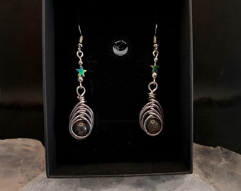 May include: A pair of silver dangle earrings with a black bead and a star charm. The star charm is iridescent green and blue.