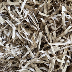 May include: Close-up of shredded brown paper packaging material. The paper is cut into long, thin strips, creating a textured, layered appearance. This eco-friendly packing filler is used for cushioning and protecting items during shipping.