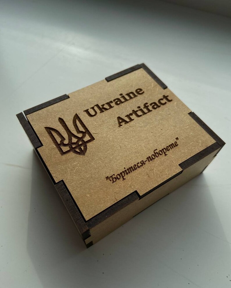 May include: A small wooden box with a brown and black finish. The box has a Ukrainian coat of arms and the text "Ukraine Artifact" on the top. The bottom of the box has the text "Борись-за-свободу" in Cyrillic.