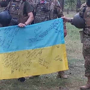 Pode incluir: Um grupo de soldados segurando uma bandeira ucraniana. A bandeira é azul e amarela e tem assinaturas escritas nela. A bandeira diz "Слава Україні!" que se traduz como "Glória à Ucrânia!" em português.