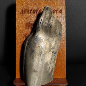 Könnte beinhalten: Ein Stück Metallpanzerung von einem russischen Fahrzeug, ausgestellt auf einer Holztafel. Die Tafel trägt ein Metallschild mit der Aufschrift "Originalteil der Panzerung russischer Fahrzeuge vom Schlachtfeld in der Ukraine".