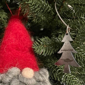 Könnte beinhalten: Ein silberner Weihnachtsbaumschmuck mit einer Silhouette eines Panzers und dem Text "From battleground in Ukraine" hängt an einem grünen Weihnachtsbaum.