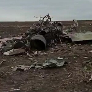 May include: Close-up of a destroyed aircraft wreckage in a field. The aircraft is broken into pieces, with the cockpit section visible. The wreckage is scattered across the field, with debris and metal parts visible.