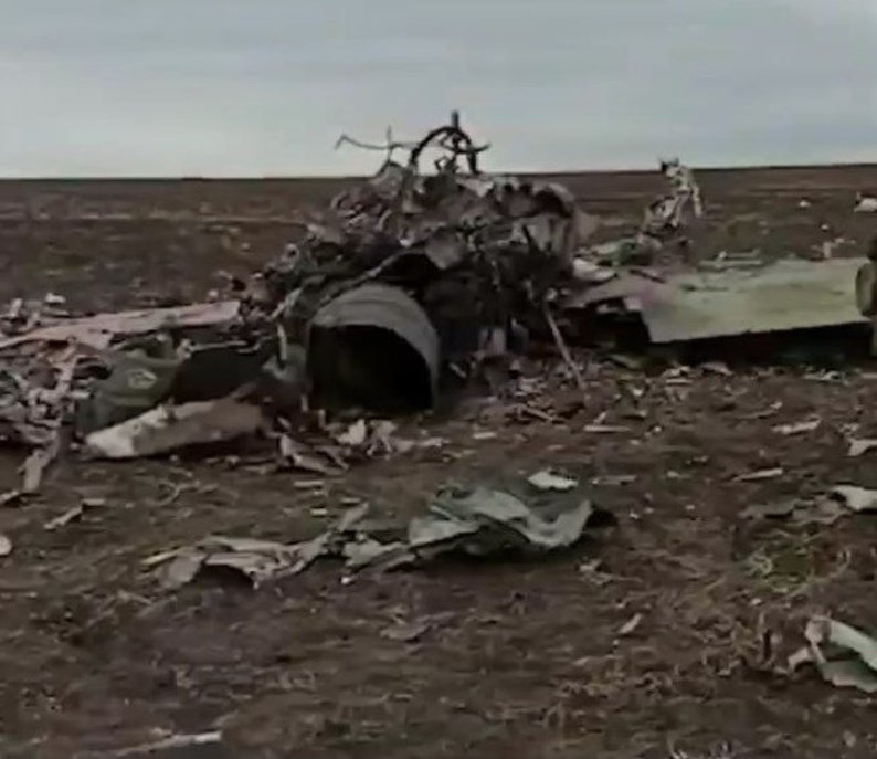 May include: Close-up of a destroyed aircraft wreckage in a field. The aircraft is broken into pieces, with the cockpit section visible. The wreckage is scattered across the field, with debris and metal parts visible.