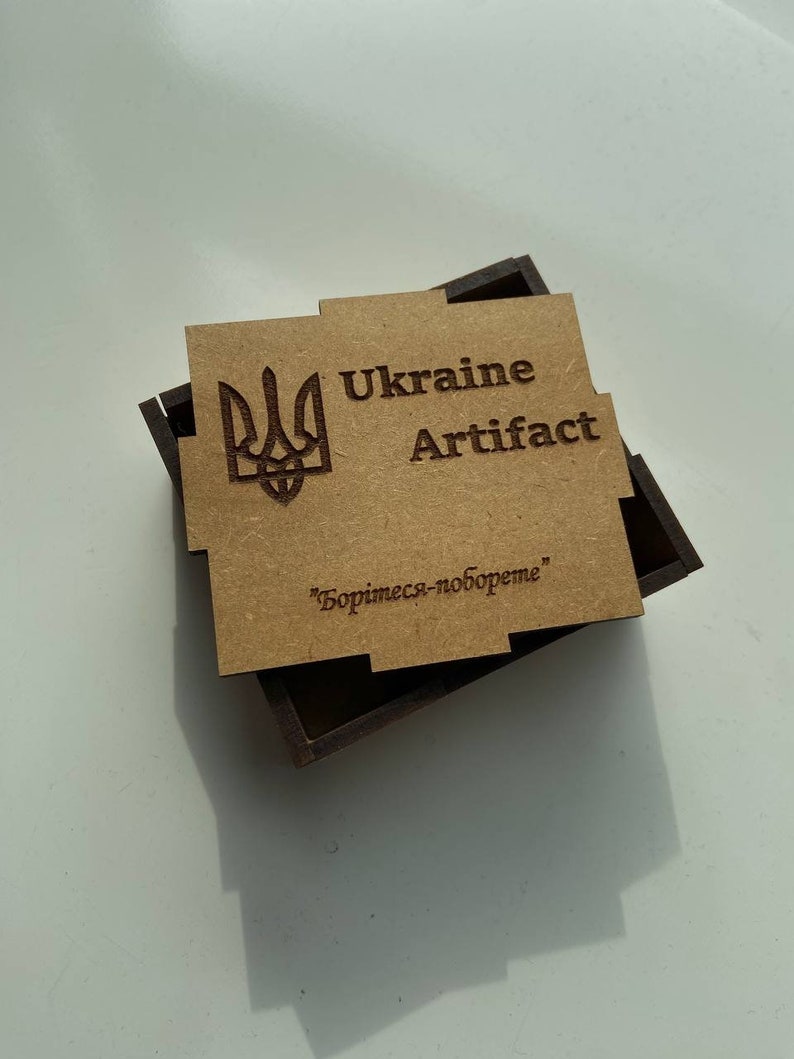 May include: A wooden box with a brown lid featuring a Ukrainian coat of arms, the words "Ukraine Artifact" and the text "Боримесь-побореме".