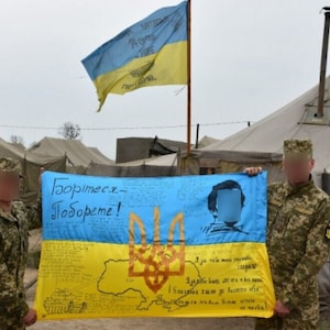 以下が含まれることがあります： ウクライナの紋章と「Зоорімєєс - Зобореме！ 」という文字が書かれた、大きく青い黄色の旗を2人の兵士が持っています。旗は、戦車、ウクライナの地図、人物の肖像画が描かれた装飾が施されています。