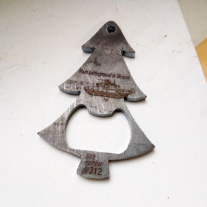 Könnte beinhalten: Ein Metall-Flaschenöffner in Form eines Weihnachtsbaums. Der Öffner trägt die eingravierten Texte "From battleground in Ukraine" und "Unit number 312" sowie ein Bild eines Panzers. Der Öffner ist aus Metall.