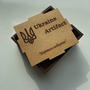 May include: A wooden box with a brown lid and a brown base. The lid has a laser-engraved image of the Ukrainian coat of arms, the words "Ukraine Artifact" and the text "Борись-за-вобoдне" in Cyrillic.