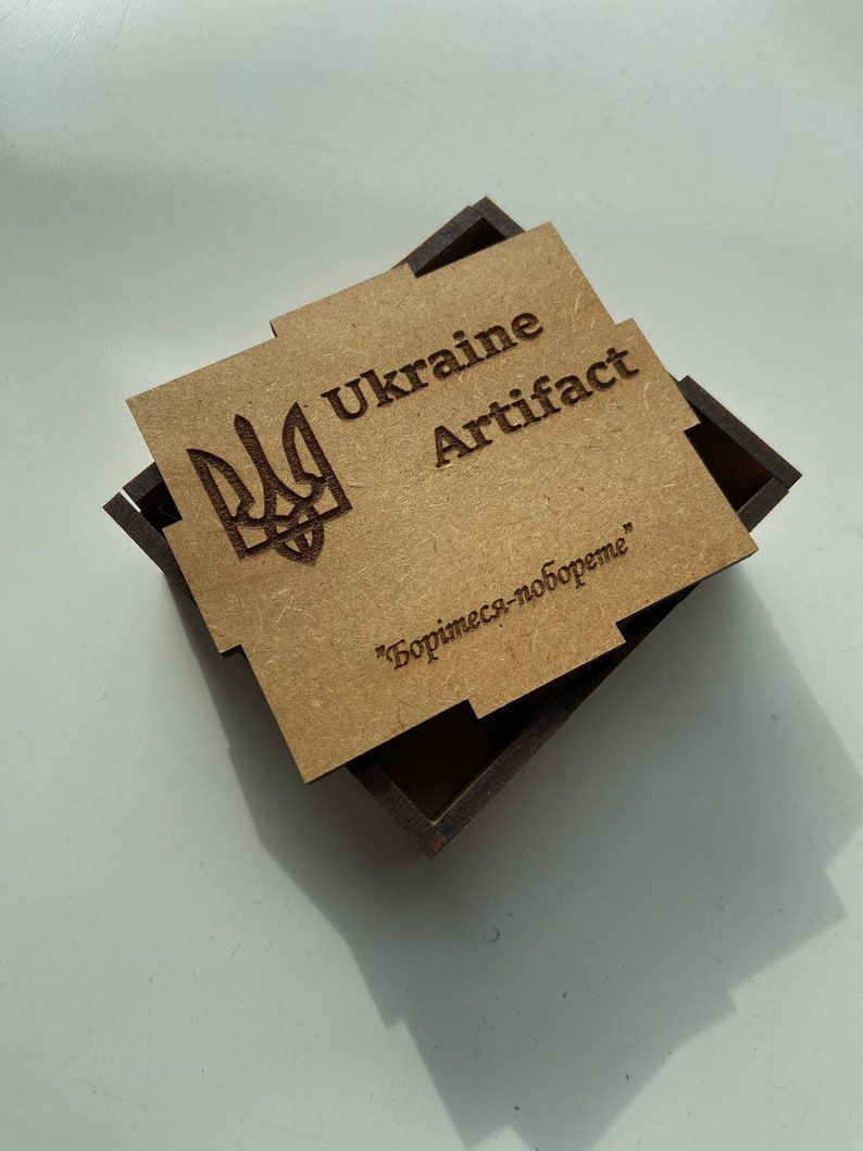 May include: A wooden box with a brown lid and a brown base. The lid has a laser-engraved image of the Ukrainian coat of arms, the words "Ukraine Artifact" and the text "Борись-за-вобoдне" in Cyrillic.