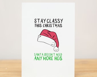 May include: A white card with a green and black text that reads "Stay Classy This Christmas. Santa Doesn't Need Any More Hos."  A red and white Santa hat is illustrated above the text.