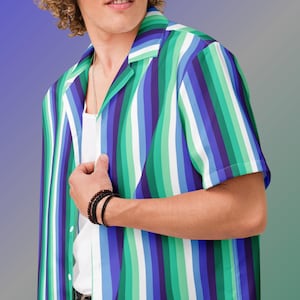 May include: A short-sleeved, button-down shirt with vertical stripes in shades of green, blue, purple, and white. The shirt has a camp collar and is worn over a white undershirt. The person is wearing a black bracelet.