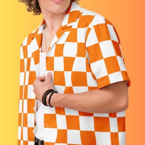 May include: Orange and white checkered short-sleeve shirt. The shirt has a classic collar and button-down front. The shirt is paired with a white undershirt and a silver necklace. The person is wearing a black bracelet.
