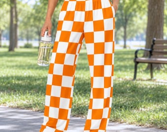 Peut inclure: Pantalon de détente taille haute avec un motif à carreaux orange et blanc. Le pantalon présente une coupe large et décontractée avec une taille élastique et des poches latérales, accompagné de baskets blanches et d'une gourde transparente.