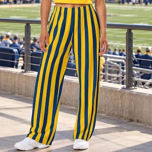 May include: Full-length trousers featuring a bold vertical striped pattern in alternating bright yellow and deep navy blue. The pants have a relaxed, straight-leg fit with a high-waisted elastic waistband and are paired with white athletic sneakers.