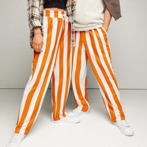 May include: Orange and white striped pants with a drawstring waist. The pants have vertical stripes and are paired with white sneakers. The overall style is casual and comfortable.