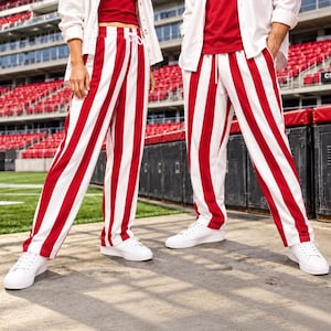 May include: Full-length trousers featuring bold vertical red and white stripes. The pants have an elasticized waistband with a white drawstring cord and a relaxed, straight-leg fit. These trousers are paired with white sneakers.