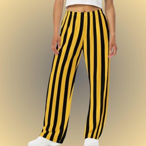 May include: Wide-leg pants with vertical black and yellow stripes. The pants have a high waist and a relaxed fit. The fabric appears to be lightweight and suitable for casual wear. The pants are paired with a white top and white sneakers.