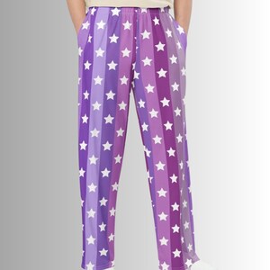 Puede incluir: Pantalones de pijama con estampado de estrellas moradas y blancas. Los pantalones presentan rayas verticales en tonos de morado, cada una adornada con estrellas blancas. Tienen bolsillos y un ajuste relajado. (Medidas en cm)