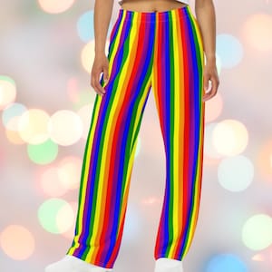 May include: Rainbow striped pants with vertical bands of red, orange, yellow, green, blue, and purple. The pants have a wide leg design and are made of a soft, flowing fabric. The pants are shown with white shoes and a white top.