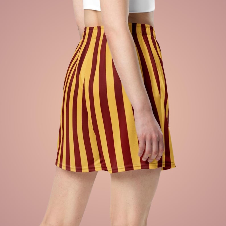 May include: A yellow and maroon striped skirt. The skirt features vertical stripes in alternating colors of yellow and maroon. The skirt is a mini-skirt style, with a fitted waist and a flared hemline. The fabric appears to be smooth and lightweight.
