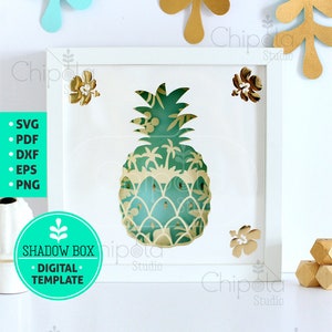 Pode incluir: Uma moldura branca com um design de caixa de sombra de abacaxi verde e amarelo. A moldura está sobre um fundo branco com folhas douradas e azuis. O texto "SHADOW BOX DIGITAL TEMPLATE" está em um círculo turquesa.